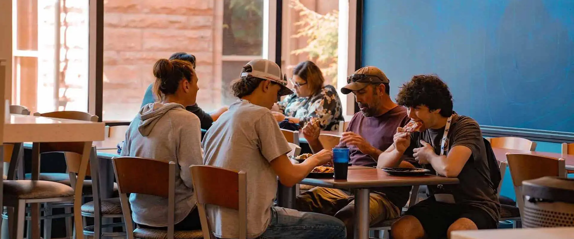 Students having a meal at a communal table with large windows in the background