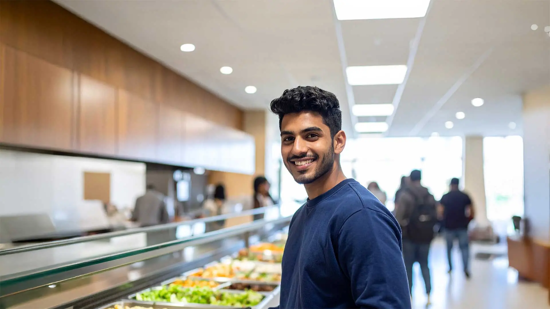Student smiling while standing in the middle of cafeteria